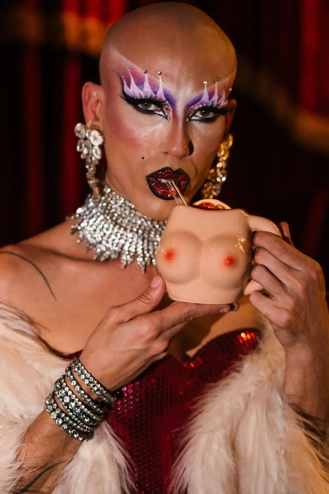 Artist in a red sequinned dress with a winking cocktail cup